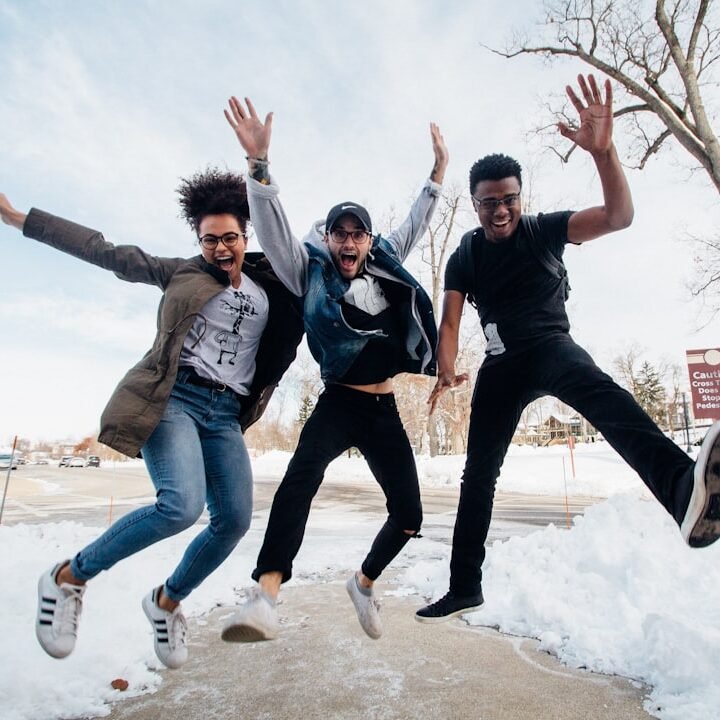 photo of three men jumping on ground near bare trees during daytime